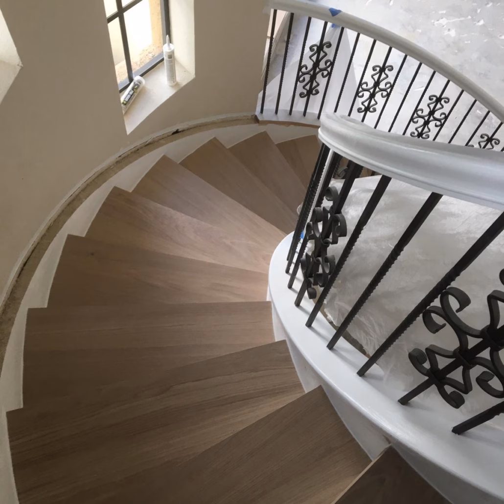 jelin Woodura Powder White Oak hardened wood flooring custom installed on a curved staircase with white risers and iron railings.