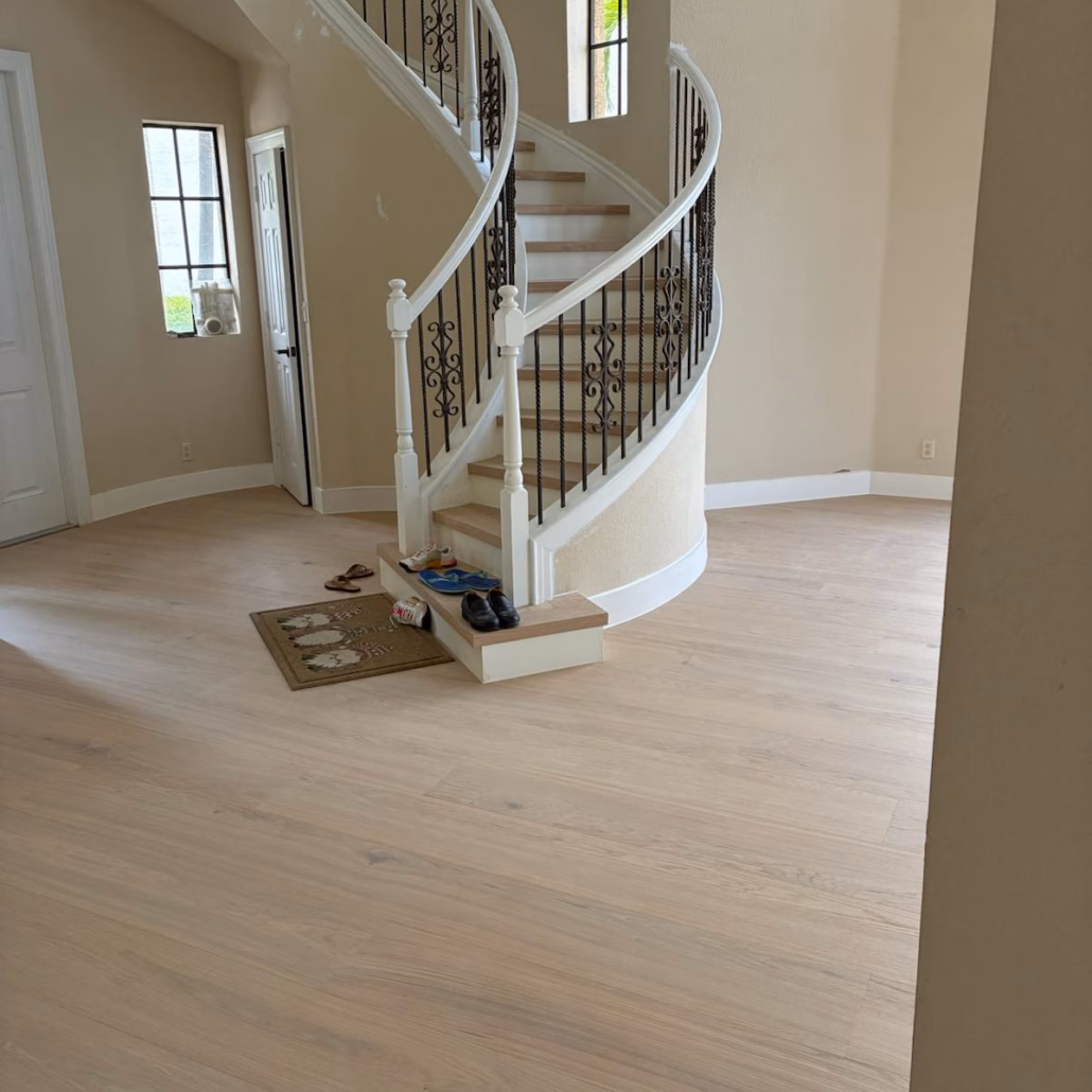 Wide foyer view showing Bjelin Woodura Powder White Oak hardened wood flooring seamlessly extending onto a grand curved staircase in a South Florida home.