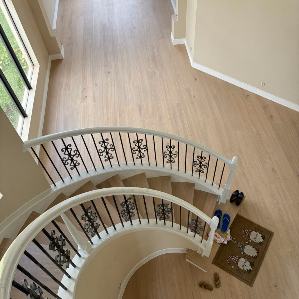 Top-down view from the upper landing of a custom curved staircase and foyer featuring Bjelin Woodura Powder White Oak hardened wood flooring.